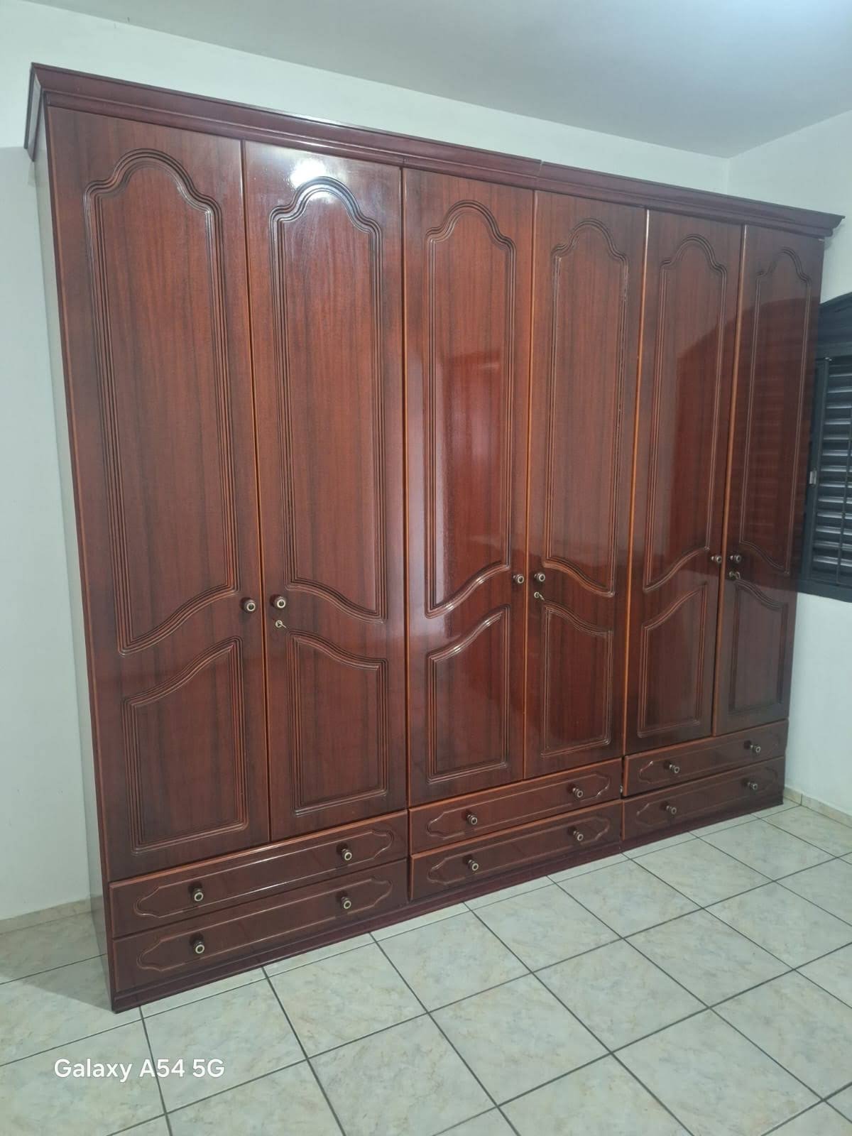 Guarda-roupa de madeira escura com portas trabalhadas e gavetas inferiores