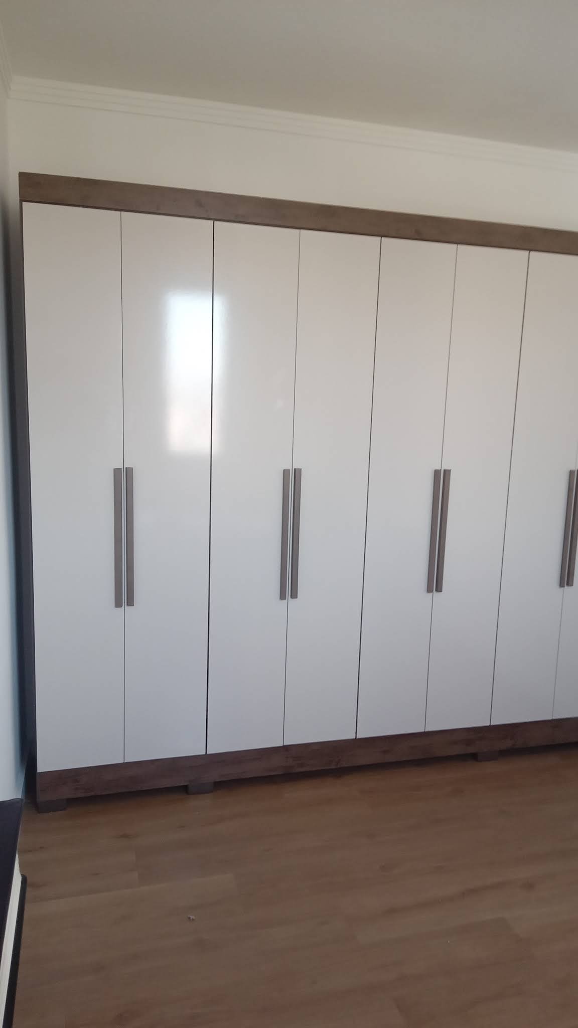 Guarda-roupa branco de portas de abrir instalado em quarto com piso de madeira